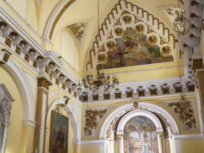 ...e infine nella chiesa. Ci troviamo in un ambiente riccamente ornato e coperto da volte a botte color ocra, con lunette con floreali bianche e brune, da cui scendono piccoli lampadari di cristallo